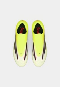 Φωτεινά κίτρινα ποδοσφαιρικά παπούτσια με αδιάσπαστο σχέδιο, που διαθέτουν μαύρες ρίγες και κόκκινες λεπτομέρειες. Υφή από πάνω με άνετη εφαρμογή για ευχέρεια κινήσεων.