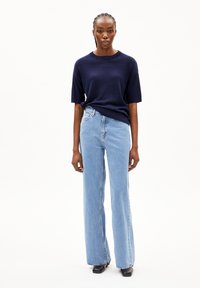 Marineblauwe geribbelde sweater met korte mouwen gecombineerd met lichtblauwe wijde spijkerbroeken. Zwarte schoenen en minimaal zichtbare hardware. Eenvoudig, strakke uitstraling.