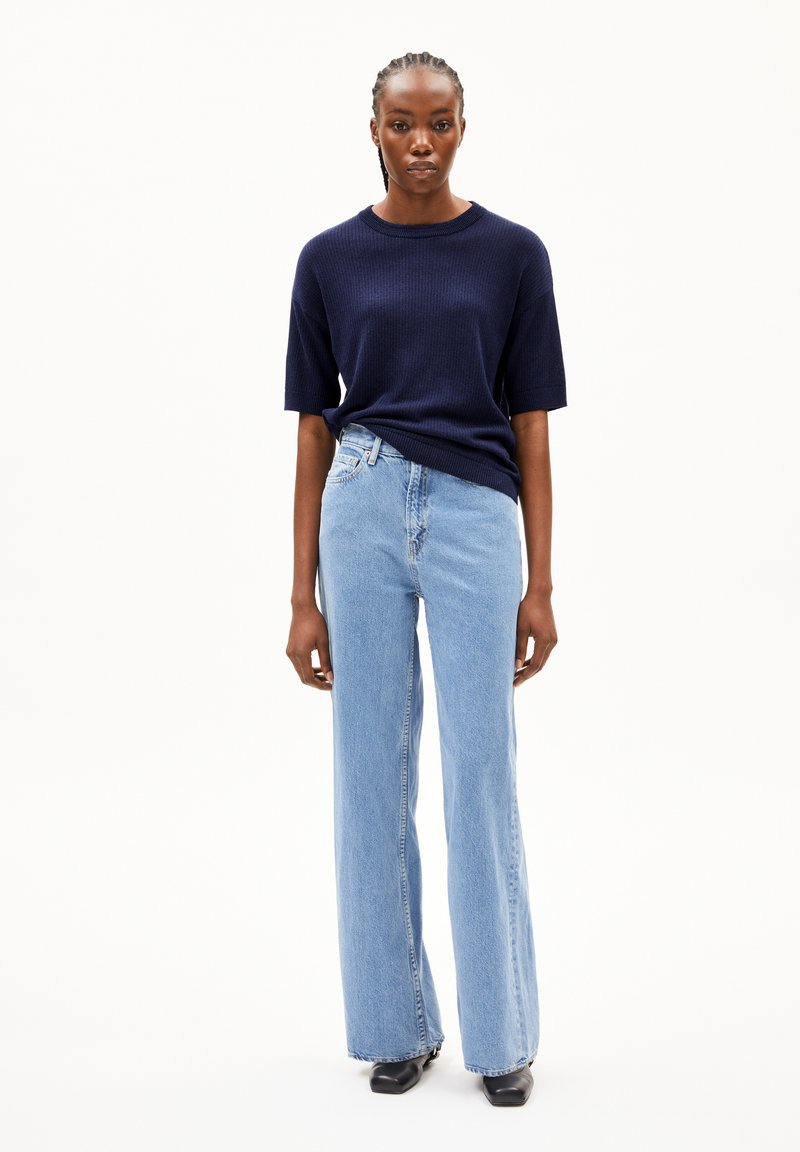 Marineblauwe geribbelde sweater met korte mouwen gecombineerd met lichtblauwe wijde spijkerbroeken. Zwarte schoenen en minimaal zichtbare hardware. Eenvoudig, strakke uitstraling.