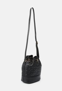 Czarna pikowana torebka w kształcie wiadra o teksturowanej powierzchni, ze złotymi elementami z oczkami, regulowanym paskiem oraz ściąganym zamknięciem na górze.