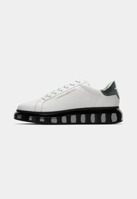 Adidași albi cu un superior neted, talpă chunky neagră, brida albă deschisă și brandul argintiu "KARL LAGERFELD" pe lateral.