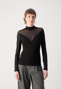 Top lungo nero a maniche lunghe con scollatura in rete trasparente a forma di V e corpo solido. Texture liscia, stile minimalista, senza motivi visibili.