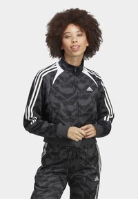Black and gray athletic jacket with a textured camo pattern, white shoulder accents, full zipper, and classic three-stripe design.