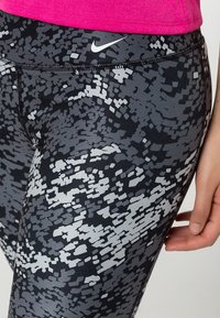 Svarta och grå mönstrade leggings med en glansig finish och en åtsittande design, med en vit Nike-logotyp på midjebandet.