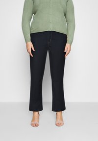 Vaqueros de mezclilla azul oscuro con pierna recta, combinados con un cárdigan de canalé verde claro y sandalias beige. Botones visibles en el cárdigan.