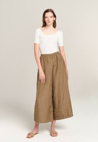 White fitted bodysuit with short sleeves, paired with loose, wrinkled brown wide-leg pants. Flat beige braided sandals complete the look.