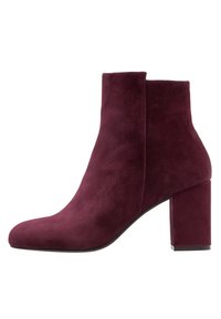 Bottine en suede bordeaux avec un haut talon bloc, un embout arrondi et une silhouette épurée. Présente des coutures minimales et un design avec découpes sur les côtés.