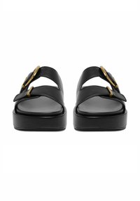 Sandalias de plataforma de cuero negro con dos tiras anchas y grandes hebillas doradas, mostradas desde una vista frontal sobre un fondo blanco.