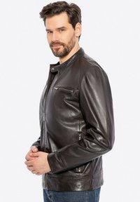 Ciemnobrązowa skórzana kurtka z zapięciem na zamek, okrągłym kołnierzykiem, bocznymi kieszeniami oraz eleganckim, dopasowanym krojem. Gładka tekstura i minimalistyczne akcenty.