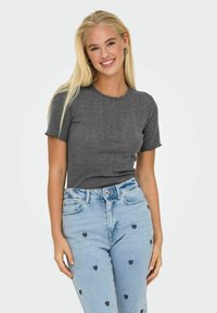 Grå tætsiddende t-shirt med korte ærmer og bølgede kanter. Sammen med lyseblå jeans, der har små sorte hjerte-mønstre og en denim struktur.