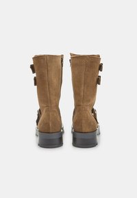 Pruun nubukist pahkluu saapad mati pindalaga, millel on külgedel kaks rihma ja pandlat ning tekstureeritud kummitald.