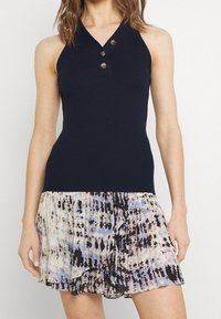 Top de canalé en color marino con escote en V y tres botones decorativos, combinado con una falda plisada que presenta un patrón de teñido anudado en azul claro y negro.