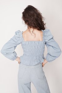 Jasnoniebieska bluzka w stylu dżinsowym z bufkami i marszczonym korpusem. Posiada falbany przy dekolcie i rękawach. Gładka tekstura, dopasowany krój.