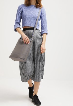 Femme portant un pull court bleu, une jupe midi plissée grise, des baskets noires et un sac à bandoulière gris.
