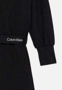 Fekete kapucnis pulóver, enyhén textúrált anyagból, rugalmas mandzsettákkal és derékpánttal, amelyen fehér "Calvin Klein" logó található.