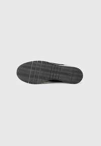 Semelle de chaussure noire avec des motifs de crampons ondulés et des rainures horizontales sur un fond blanc.