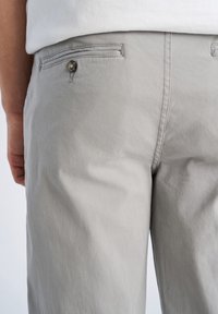 Hellgraue Baumwollhose mit glatter Textur, ausgestattet mit einer hinteren Tasche mit Knopfverschluss und dezenten Ziernähten.