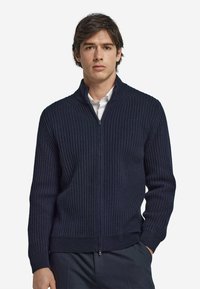 Pull zip-up bleu marine côtelé en maille texturée, avec un col montant et une silhouette ajustée.