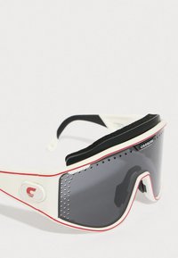 Aurinkolasit, joissa on valkoinen ja punainen kehys, suuret harmaat linssit, karhennettua mustaa pehmustetta päällä ja ilmanvaihtorei'ät sivuilla.