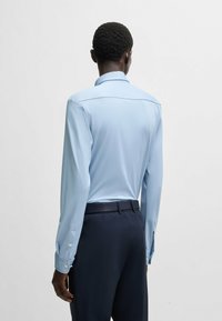 Chemise bleu clair à manches longues avec un design ajusté, couture de yoke dans le dos et poignets à boutons, assortie à un pantalon noir taillé.