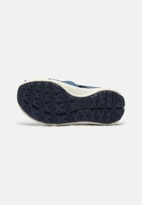 Blå sandal med en texturerad gummisula, som har en vit mellansula och ett mönstrat grepp för ökad stabilitet.