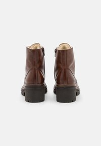 Stivali ankle in pelle marrone con una finitura liscia, cerniere laterali e una robusta suola in gomma nera con un motivo di battistrada testurizzato.