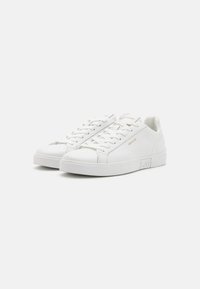 Hvite lær sneakers med lavt design, flate hvite snøringer, rund tå og diskret logo på siden og hælen.
