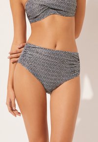 Bikiny s vysokým pasem, s černobílým pruhovaným vzorem, vyrobené z měkké látky, se shromážděnou texturou v oblasti pasu pro zvýraznění designu.