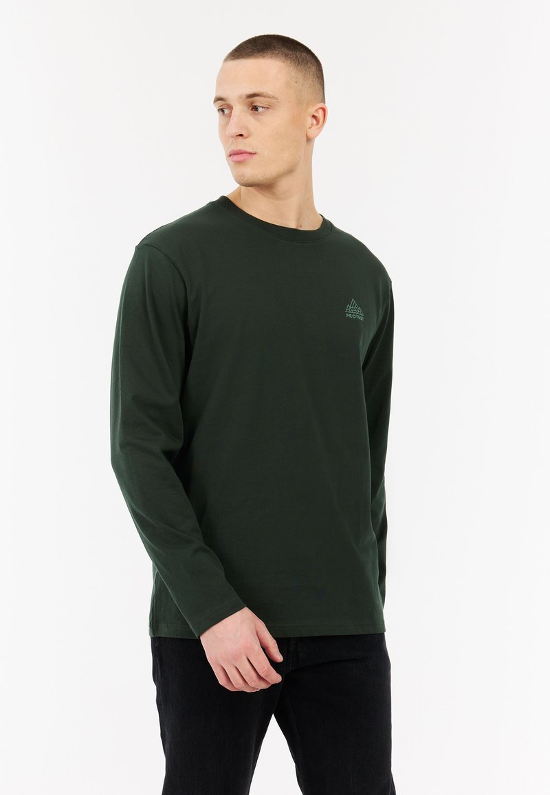 Donkergroen katoenen t-shirt met lange mouwen en een ronde hals. Heeft een klein, lichtgroen logo op de linkerborst. Sluit strak aan.