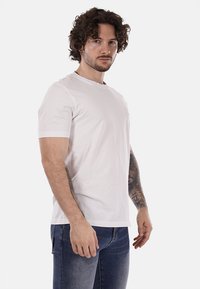 Maglietta in cotone bianco con maniche corte, scollo rotondo e dettaglio logo discreto sul petto; abbinata a jeans in denim blu.