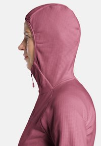 Giacca con cappuccio in un colore rosa tenue, realizzata in tessuto testurizzato con un design aderente. Presenta una cerniera e una costruzione senza cuciture per il comfort.