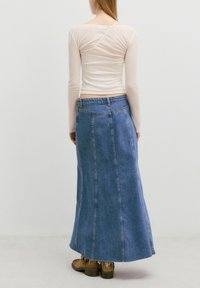 Lichtbeige lange mouwtop gecombineerd met een blauwe denim maxi-rok, met een rechte snit, een middelhoge taille en een rafelige zoom. Bruine schoenen zichtbaar.