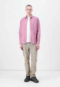 Light pink button-up shirt over a white t-shirt, paired with light beige pants and black sneakers. Simple design and casual fit.