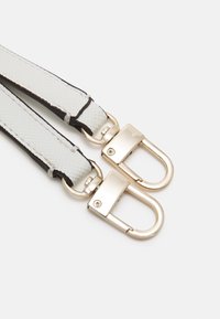 Hvite teksturerte lærsener med gulltonede metallsnapskroker vedhæftet på en hvid baggrund.