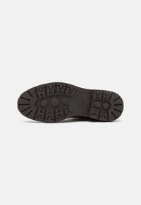 Suela de zapato de goma negra con diseño de textura en relieve, que presenta patrones circulares y angulares, con el logotipo de la marca grabado cerca del talón.