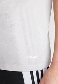 Svetlošedé tričko z materiálu odvádzajúceho vlhkosť s textúrovanou tkaninou. Obsahuje logo "AEROREADY" v bielej farbe na leme, v kombinácii s čiernymi športovými šortkami.