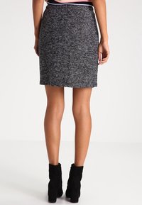 Stickad svart och vit kjol med rak klippning, strukturerad tyg och midjehöjd, i kombination med svarta ankelstövlar.