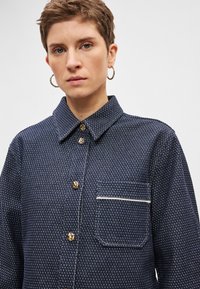 Μπλε σκούρο πουκάμισο με κουμπιά, με υφή σχεδίου, διαθέτει χρυσούς κουμπιά, τσέπη στο στήθος με λευκή επένδυση και κλασικό γιακά.