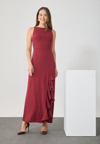 Burgunderfarbenes ärmelloses Kleid mit tailliertem Oberteil, fließendem Rock und gerafftem Saumdetail. Hergestellt aus glattem, dehnbarem Stoff. Die Absätze ergänzen den Look.