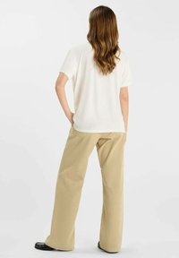 Witte T-shirt met korte mouwen in combinatie met beige wijde broek. De stof lijkt zacht met een gladde textuur. Eenvoudig, minimalistisch ontwerp.