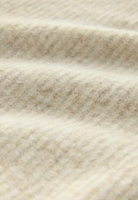 Blød uldne stof i cremefarve med et struktureret ribbet mønster, der viser subtile nuancer i farven og en indbydende fuzzy overflade.