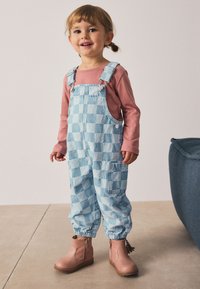 Lyseblå ternede denimoveralls med justerbare stropper, sidelomme, elastiske manchetter, kombineret med pink langærmet skjorte og brune støvler.