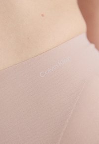 Lyse rosa leggings laget av teksturert stoff. Har en diskret Calvin Klein-logo trykket nær midjen. Glatt og tilpasset design.