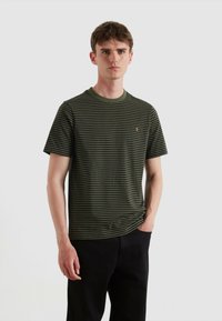 Camiseta de manga corta a rayas verdes y negras con cuello redondo acanalado y pequeño logotipo dorado en el pecho. Material de algodón suave.