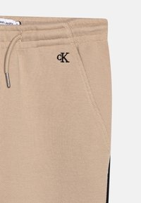 Beiga joggers i strukturerad tyg, med justerbar dragsko, sidfickor och en svart panel längs den yttre sömmen.