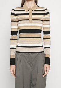 Rippiertes langärmliges Polo-Shirt mit einem beigen, schwarzen und weißen gestreiften Muster, ausgestattet mit einem beigen Kragen und einer Knopfleiste am Hals.