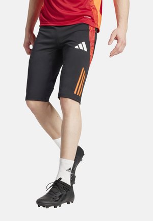 Zwarte sportshorts met oranje accenten, gemaakt van elastisch materiaal, met een nauwsluitende pasvorm en drie verticale strepen aan de zijkant.