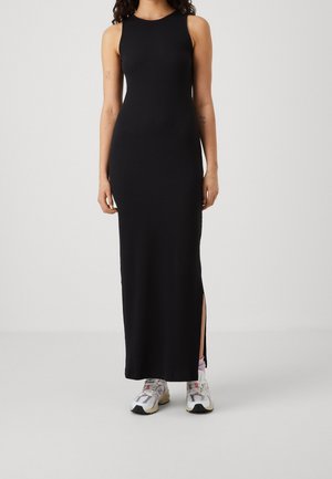Robe maxi noire sans manches avec une silhouette ajustée et une fente sur le côté. Associée à des baskets colorées. Texture lisse, design minimaliste.