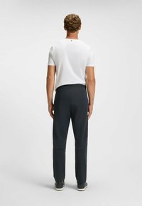 Herroutfit som består av en vit kortärmad skjorta och mörkgrå sportbyxor, tillverkade av ett smidigt, elastiskt material med en figurnära design.