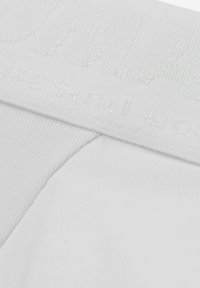 Ceinture en coton blanc avec texte en relief. Texture lisse et maintien sécurisé. Détail des coutures visible, mettant en avant la fonctionnalité du design.